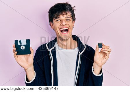 Handsome hipster young man holding floppy disk and sdxc card celebrating crazy and amazed for success with open eyes screaming excited. 