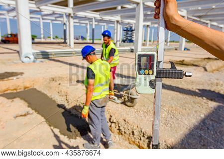 Construction Worker Is Holding Leveling Rod To Help Surveyor, Geodesist To Measure Position, Depth.