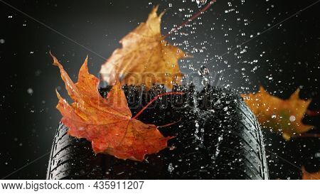 Car tire with falling autumn leaves and splashing water, macro photo, weather concept. Studio photo, Free space for text.
