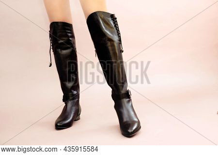 Caucasian Female Legs In Sexy Black Leather High Long Boots Jackboots On Light Pink Beige Background