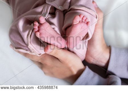 Adorable Newborn Caucasian Baby Girl Legs In Pink Jumpsuit. Little Girls Pink Heels . Top View. Clos