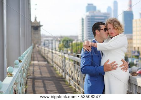 Pregnant woman in white and stylish man embrace outdoor in city.
