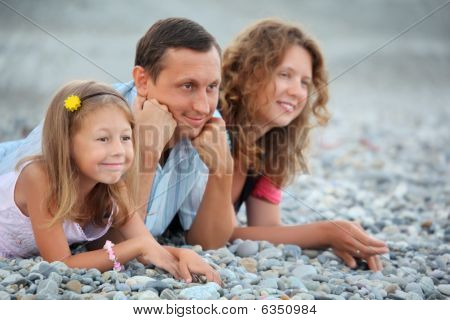 Lykkelig familie med lille pige liggende på stenede strand