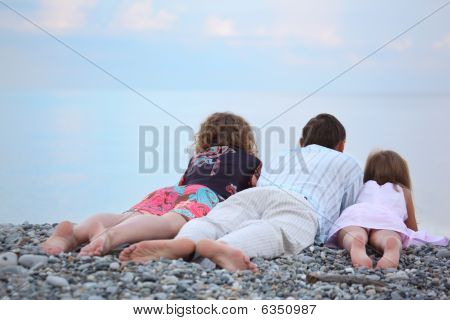 Lykkelig familie med lille pige liggende på stenede strand, liggende tilbage