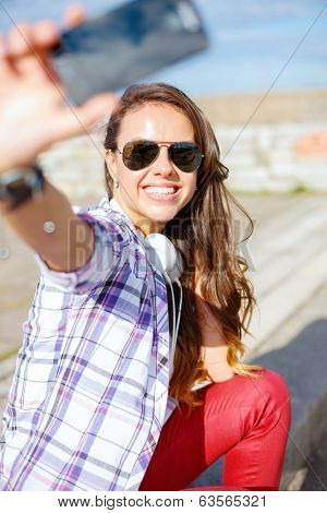 holidays and tourism concept - smiling teenage girl taking picture with smartphone camera aoutdoors