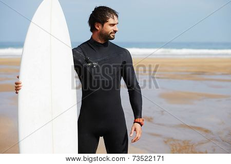 Beautiful surfer man with surfing board looking along the shore