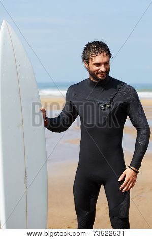 Young professional surfer smiling standing on beautiful ocean beach with his white surfboard