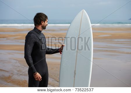 Handsome brunette surfer holding his board stand on the beach waiting waves