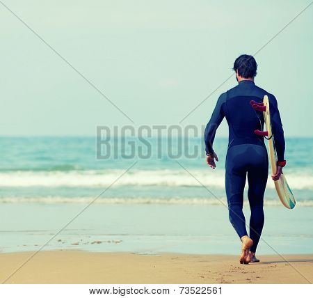 Professional surfer man dressed in wetsuit ready to surfing on big waves walking on the beach