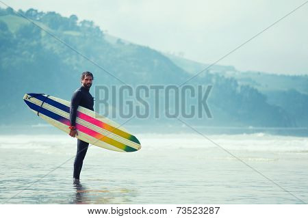 Surfer carrying surfboard while walking on the beach and looking at ocean to find the perfect spot