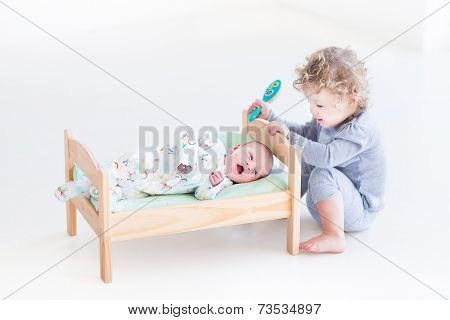 Funny Curly Toddler Girl Playing With Hew Newborn Baby Brother In A Toy Bed Trying To Brush His Hair