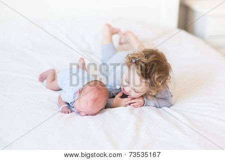 Sweet Toddler Girl Supporting Her Newborn Baby Brother During His Tummy Time On A White Bed