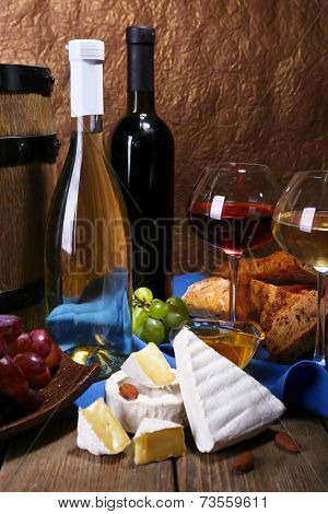 Supper consisting of Camembert and Brie cheese, honey, wine and grapes on napkin in basket and wine barrel on wooden table on brown background