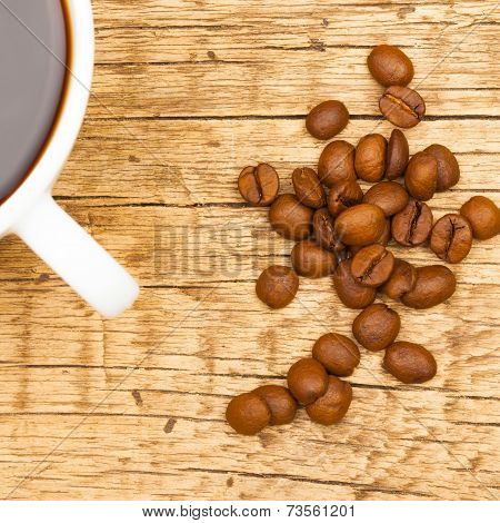 Close Up Of White Ceramic Coffee Cup With Roasted Coffee Beans On Wooden Table - View From Top