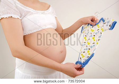 Close up on pregnant belly with baby clothes.