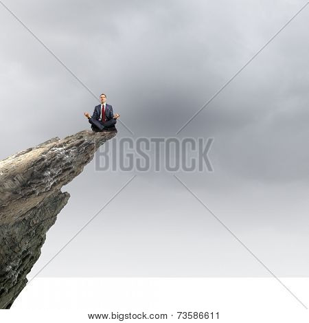 Young businessman sitting lotus pose on edge of rock mountain