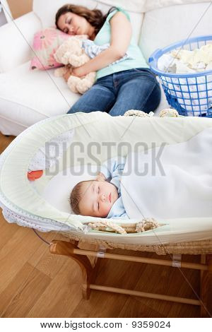 Junge Mutter auf dem Sofa zu schlafen, während ihr Baby In seiner Wiege im Wohnzimmer schläft