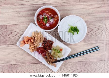 Rice gruel and  side dish  on wood. (Dried shredded pork, Chinese sausage, crispy fish, sausage, fried baby clams, sliced red onion, pickle Chinese cabbage, Spicy sardine salad and shallots )