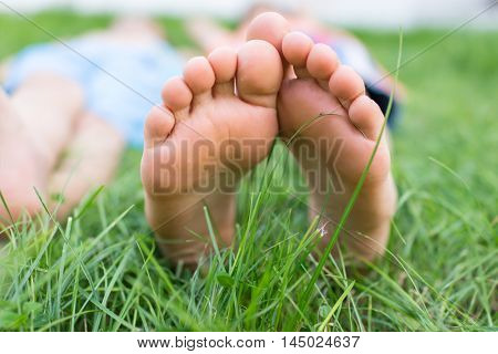 Group of happy children feet lying on green grass outdoors in summer park