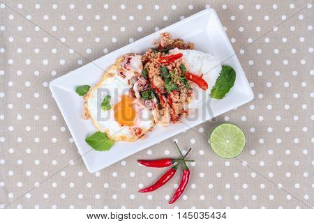 Rice topped with stirred  minced-pork ,squid ,basil and fried egg(sunny up) on brown napery.