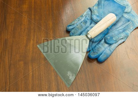 paint scraper with wood handle and working gloves on wooden.