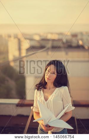 Beautiful young girl at the roof with origami paper crane in hands. Vintage tinted selective focus.