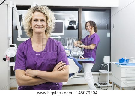 Assistant Standing Arms Crossed With Colleague Working In Dentis