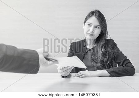 Closeup asian working woman receive work document from her boss with unwilling face in meeting room on blurred wooden desk and wall textured background in work concept in black and white tone