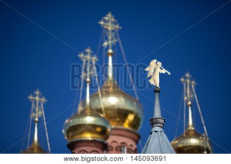 Gilded angel shaped weathervane on the steeple blurred golden domes and crosses and blue sky on background; Chernigovsky Skit Sergiev Posad Russia.