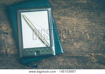 Black ereader with notebook in leather cover and ink pen on vintage old rustic wooden table. Blank E-book reader. New technologies in education. Back to school concept. Top view. Copy space.