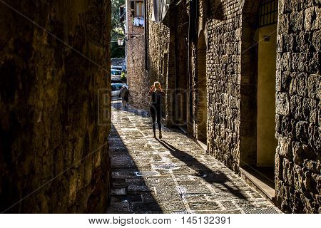 Girl walking in an alley in Italy with shadow - tuscany