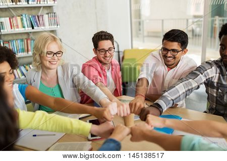 education, school, teamwork and people concept - group of international students sitting at table and making fist bump