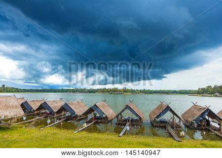 View of Huay Tung Tao Lake with food rafts around the lake and mountains and dark blue thunder storm clouds in the background