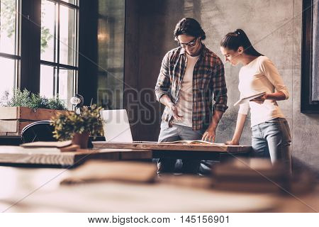 Discussing business with colleague. Confident young man and woman working together while standing near the desk in creative office