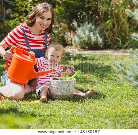 Pregnant woman with little daughter in the summer orchard cearing flower.