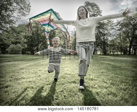 Runnings little boy and mother flies with them kite in the park under sunligt.
