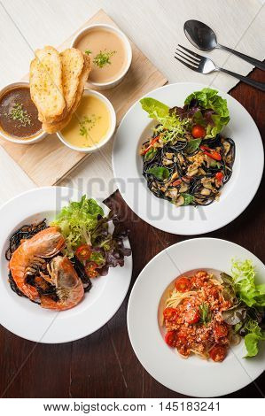 Top view of modern cuisine set including Pasta dried chili Black pasta with clams Carbonara pasta with bacon and Onion-Corn-Mushroom soup with toast on wood table in restaurant