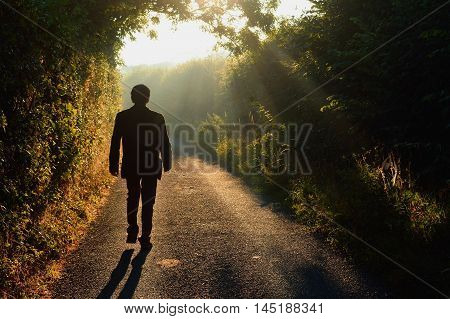 Alone man walking along a small country road in a misty morning
