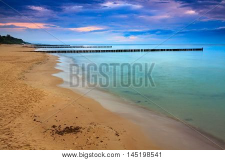 Sandy coast with dramatic sky and pier during sunset.