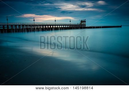 Sandy coast with dramatic sky and pier during sunset.