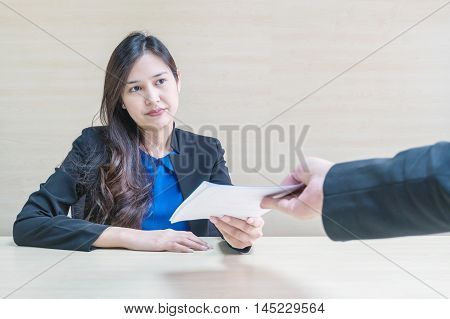 Closeup asian working woman receive work document from her boss with unwilling face in meeting room on blurred wooden desk and wall textured background in work concept