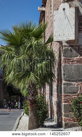Sun clock and a palm tree on the corner of Dzhuaya, Djumaya Mosque or Cuma Camii in turkish, downtown Plovdiv on a sunny summer day.
