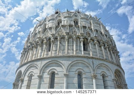 View of Baptisery building in Cathedral Square in Pisa, Italy, on cloudy blue sky background.