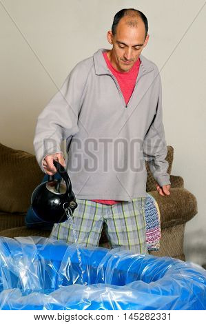 A father assists a midwife by adding hot water to a birthing pool before his son is born in it.