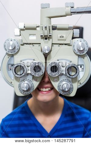 Young patient looking through phoropter during eye examination in ophthalmology clinic