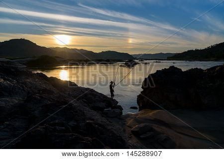 silhouette fisherman holding fishing equipment in action with sundog on blue sky background at sunset