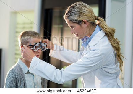 Female optometrist examining young patient with phoropter in ophthalmology clinic