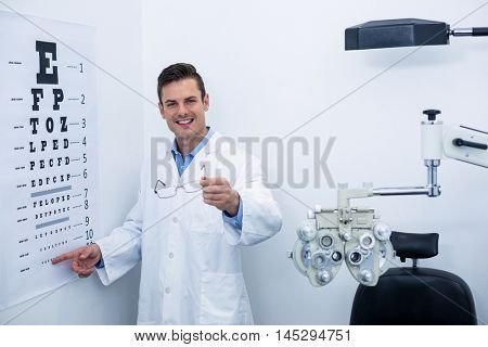 Handsome optometrist pointing at eye chart in ophthalmology clinic