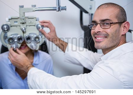 Smiling optometrist examining female patient on phoropter in ophthalmology clinic