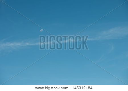 moon visible in daylight blue sky with white soft clouds